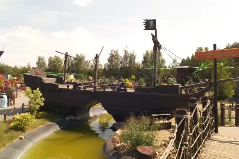 Statek piracki z czarną banderą i armatami, jak z krainy Canpol Wonderland, przecina wodny rów.