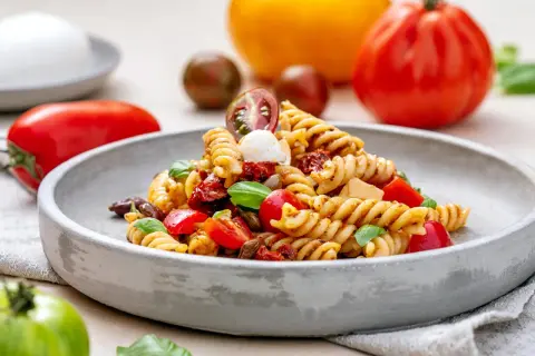 Ein köstlicher italienischer Nudelsalat mit Fusilli, Tomaten, Mozzarella und Basilikum, serviert auf einem grauen Teller.