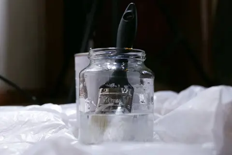 Pędzel zanurzony w słoiku z płynem, prawdopodobnie terpentyną balsamiczną, gotowy do czyszczenia.