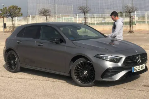 Un hombre se apoya en un elegante Mercedes Clase A gris oscuro, listo para un viaje.