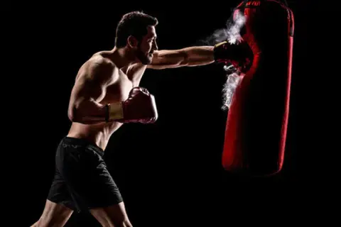 Boxer training to strengthen his chin for boxing, punching a red heavy bag with force.