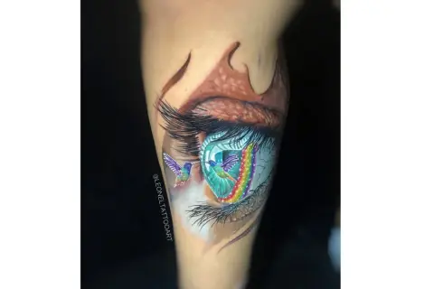 Tatuajes ojo con colibríes y arcoíris vibrantes. Un ojo realista con detalles de fantasía, como si los colibríes volaran a través de un portal de colores.