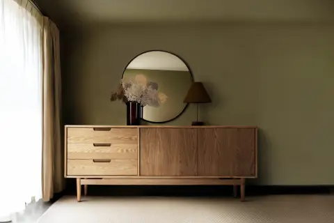 Ein Sideboard aus Holz mit Schubladen und Türen, darüber ein Spiegel und eine Lampe. So sieht ein praktisches Sideboard aus.