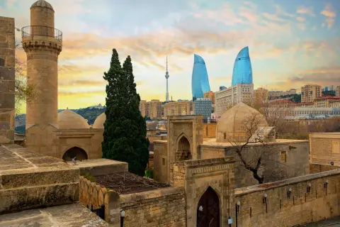 Zachód słońca nad Baku. Stare mury i minaret kontrastują z nowoczesnymi wieżowcami Flame Towers. Baku pogoda zachęca do zwiedzania.