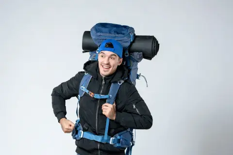 Un jeune homme souriant avec un grand sac à dos bleu, prêt pour l'aventure. On se demande : sac 70 litres combien de kilos ?