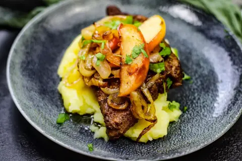 Leber Berliner Art auf Kartoffelpüree mit karamellisierten Zwiebeln und Apfelscheiben, garniert mit Petersilie.