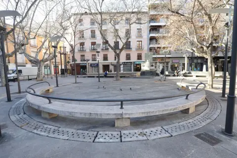 Banqueta circular de piedra en la plaza San Pedro Nolasco Zaragoza, con árboles desnudos y edificios al fondo.