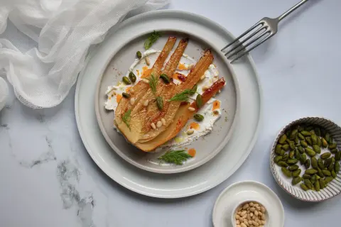 Un plat de fenouil au four, doré et tendre, servi sur une crème onctueuse, garni de pistaches, pignons et d'aneth frais.