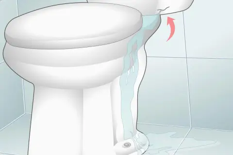 Water is leaking from a cracked toilet tank, causing low water in the toilet bowl and a puddle on the floor.