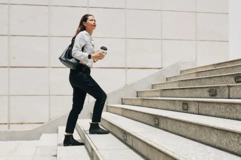 Frau steigt Treppen hoch, Kaffee in der Hand. Ein guter Weg, um abzunehmen durch gehen und fit zu bleiben.