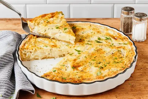 Eine köstliche Spargel Quiche wird serviert. Ein Stück wird mit einem Tortenheber herausgehoben, garniert mit frischer Petersilie.
