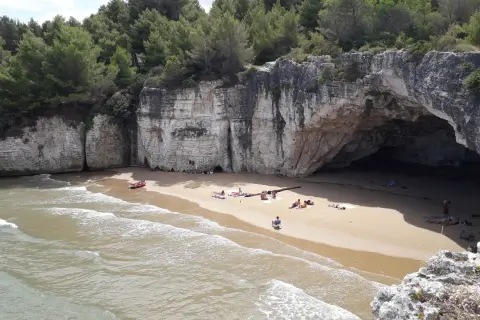 Spiaggia dei Colombi: una baia nascosta con una grotta marina, scogliere bianche e pini marittimi. Alcune persone si rilassano sulla sabbia dorata.