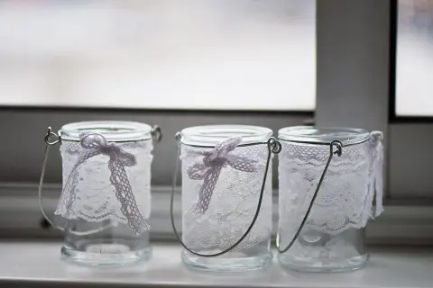 Drei hübsch gestaltete Windlichter aus Glas mit zarter Spitze und Schleifen.