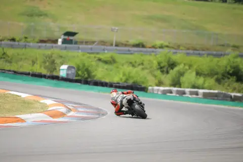 Motocyklista w czerwonym kombinezonie pochylony na zakręcie toru wyścigowego.