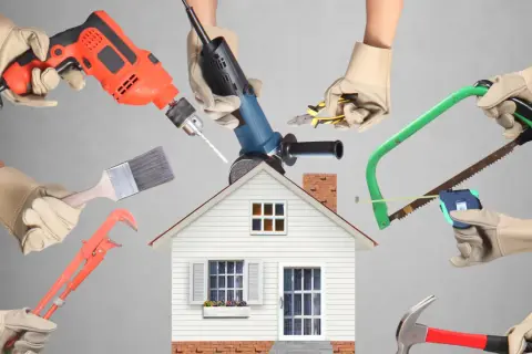 Manos con guantes sostienen herramientas de construcción alrededor de una casa. ¡Calcula tu reforma casa precio!