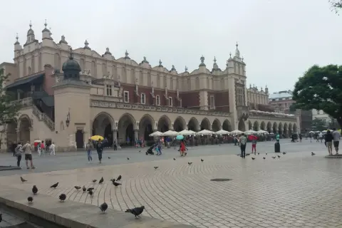 Deszczowy dzień na Rynku Głównym w Krakowie. Ludzie z parasolami spacerują, szukając schronienia w Sukiennicach lub kawiarniach. To świetny pomysł, co robić w Krakowie, gdy pada.