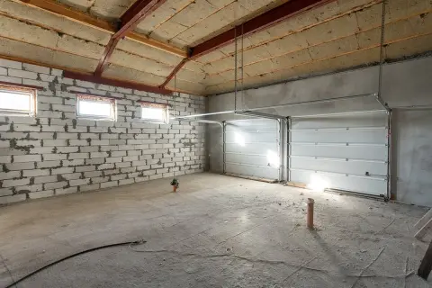 Intérieur d'un garage en construction, prêt à isoler. Murs en parpaings, plafond isolée, portes de garage sectionnelles blanches.
