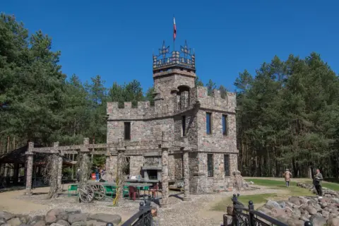 Kamienny zamek z wieżą i polską flagą, otoczony lasem. Nietypowe atrakcje Podlasia, które zaskakują.