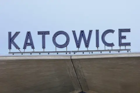 Napis KATOWICE z niebieskimi neonami na tle błękitnego nieba.