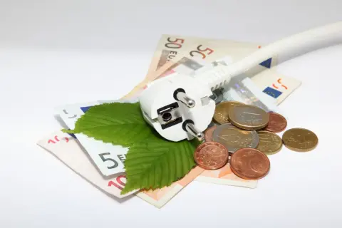 Wtyczka, liście i monety na banknotach euro symbolizują poszukiwanie, gdzie najtańszy prąd.