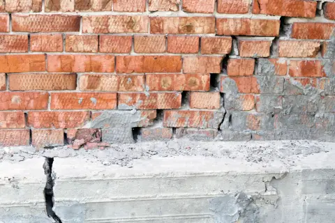 Uszkodzona ceglana ściana i pęknięty betonowy stopień świadczą o problemach z podbijaniem fundamentów.