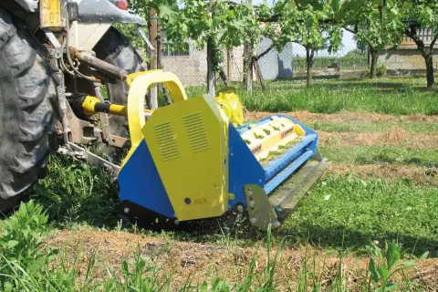 Trattore con falciatrice gialla e blu che lavora in un vigneto. L'erba tagliata copre il terreno, un segno di potenziale inquinamento del suolo se non gestita correttamente.