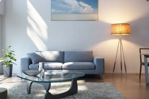 Ein helles Wohnzimmer mit grauem Sofa, Glascouchtisch und einem Bild mit Meerblick. Welche Farbe passt zu grauem Sofa? Hier sehen wir helle Töne, die gut harmonieren.