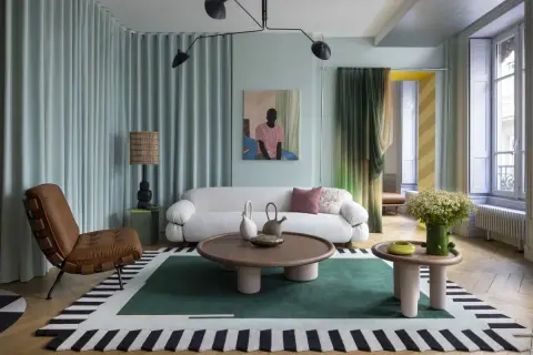 Salotto con divano bianco bouclé, poltrona in pelle, tappeto geometrico e lampada da terra, in un audace stile massimalista.