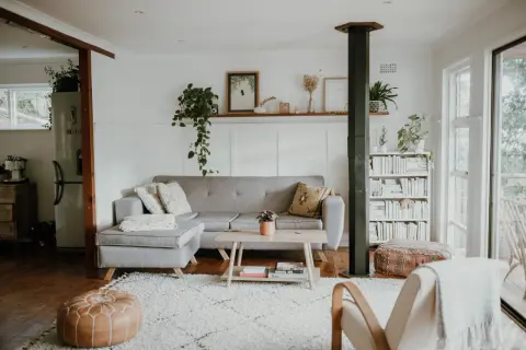 Ett ljust vardagsrum med grå soffa, träbord och bokhylla. Gröna växter och konst ger en känsla av skandinavisk minimalism.