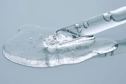 Kropla przejrzystego serum z bąbelkami powietrza spływa z pipety. To połączenie ceramidów a peptydów dla zdrowej skóry.