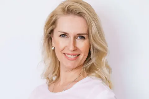 Uśmiechnięta blondynka po czterdziestce z fryzurą dodającą objętości cienkim włosom.
