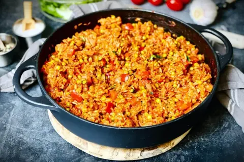 Herzhafter Djuvec Reis mit Mais und Paprika in einer Gusseisenpfanne, bereit zum Servieren.