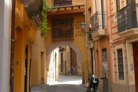 Calle estrecha con arco, fachadas amarillas y naranjas, un balcón y una moto. Descubre los **secret places Valencia**.