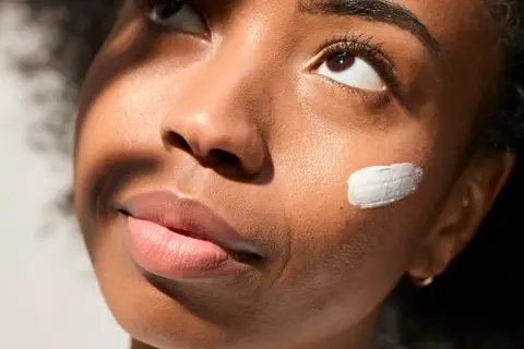 Geste doux pour mettre de la crème sur la joue d'une jeune femme, illuminée par la lumière du soleil.