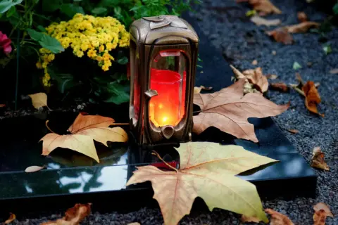 Grablicht auf einem Grabstein, umgeben von Herbstlaub und Blumen. Ein stiller Gruß zu Allerheiligen katholisch.