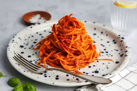 Ein Berg aus gekochte spaghetti braten mit Tomatensauce auf einem Teller mit blauen Tupfen. Eine Gabel liegt daneben.