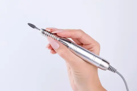 Dłoń z paznokciami trzyma srebrną frezarkę. Zastanawiasz się, jaka moc frezarki do paznokci jest potrzebna do idealnego manicure?
