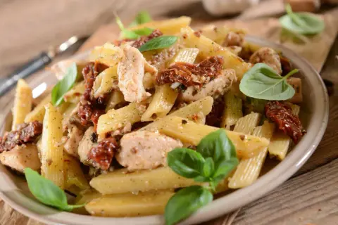 Penne z kurczakiem i suszonymi pomidorami, udekorowane świeżą bazylią. Pyszne danie na obiad.