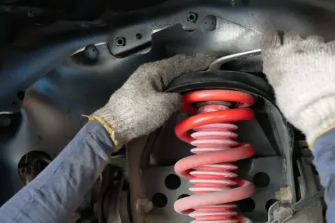Mechanik w rękawiczkach dokonuje wymiany sprężyny amortyzatora w samochodzie.