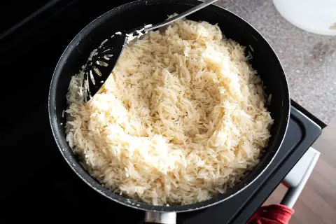 En stor kastrull med fluffigt, vitt ris står på spisen. En svart slev rör om i det nykokta riset, redo att serveras. Perfekt för en snabb middag, detta ris i kylen är en räddare i nöden.