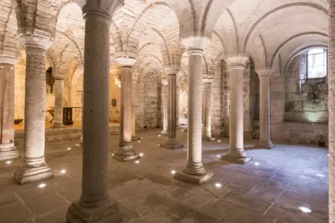 Cripta dell'Abbazia di San Salvatore, con colonne in pietra e volte a crociera illuminate da faretti a pavimento.