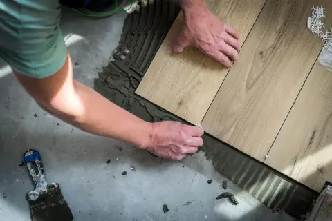 Man placing wood-look tiles on cement floor. Learn como colocar el parquet horizontal o vertical para un acabado perfecto.