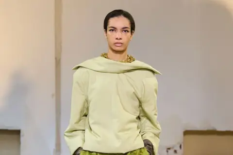 Mannequin portant un haut ample couleur matcha, avec un collier doré audacieux et une jupe texturée verte.