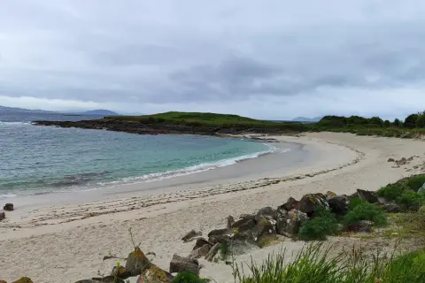 La serena playa Santa Marta de Cangas, con sus aguas turquesas y arena dorada, invita a la calma bajo un cielo nublado.