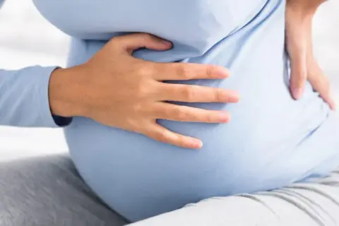 Kobieta w ciąży trzyma się za bok, odczuwając ból sugerujący kolkę nerkową w ciąży.