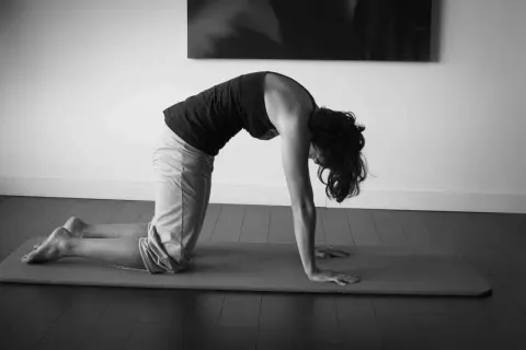 Une femme effectue un étirement chat sur un tapis de yoga, courbant son dos et rentrant sa tête.