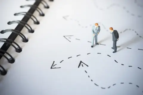 Figurki biznesmenów analizują ścieżki na mapie, symbolizujące bariery wejścia na rynek i strategie ich pokonywania.