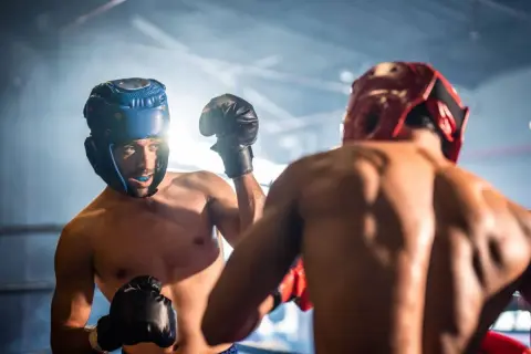 Two boxers in a ring, wearing headgear and gloves, engage in sparring. The intense training session highlights their focus and determination.