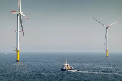 Ogromne turbiny wiatrowe na morzu, symbol nowoczesnej morskiej energetyki wiatrowej, na tle spokojnego oceanu. Statek serwisowy płynie w kierunku jednej z nich.