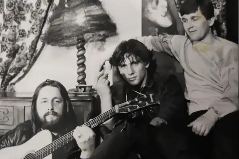 Trzech muzyków zespołu Universe pozuje z gitarami w przytulnym wnętrzu.